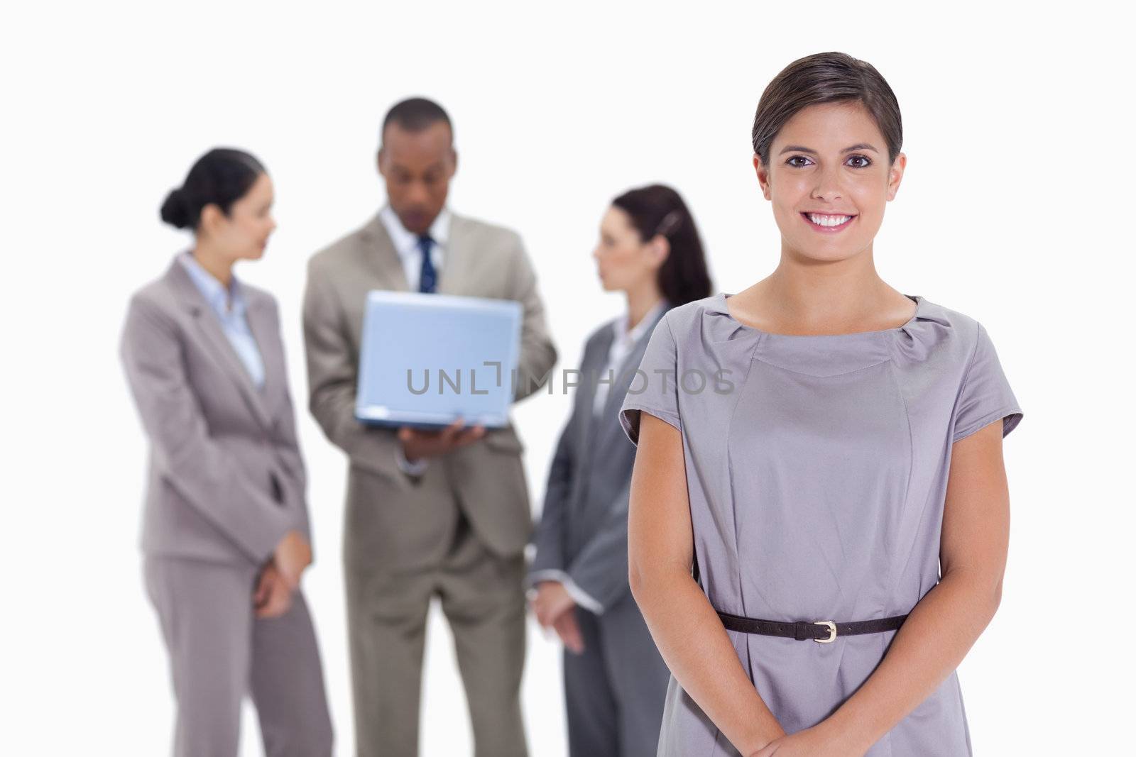 Close-up of a woman smiling with business team in the background with a laptop which a man is looking at the screen and the others are listening 