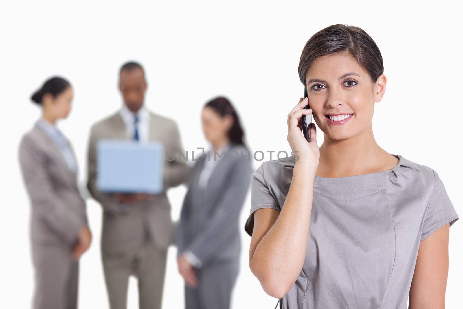 Close-up of a Woman with her head tilted slightly smiling on the phone and three co-workers with a laptop in the background