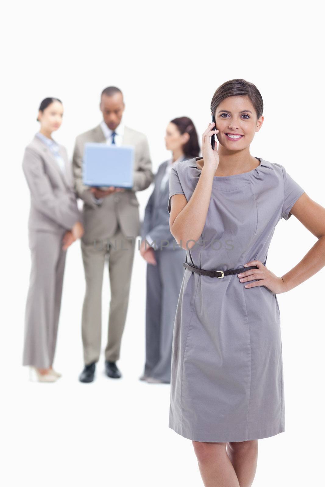 Businesswoman on the phone with a hand on her hip and crossing her legs, with co-workers in the background with a laptop
