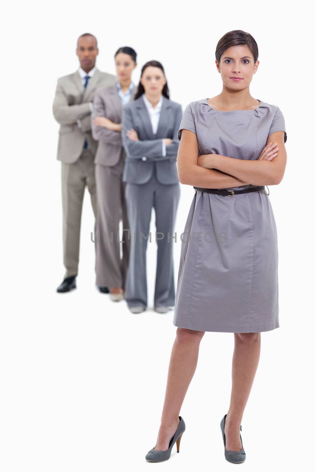 Businesswoman with a discrete smile and a team crossing their arms and standing behind each other against white background