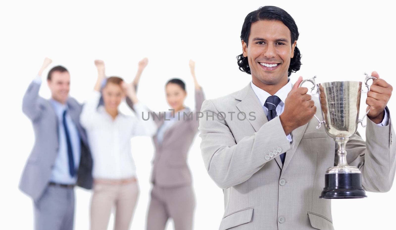 Close-up of a businessman smiling and holding a cup with people cheering behind him against white background