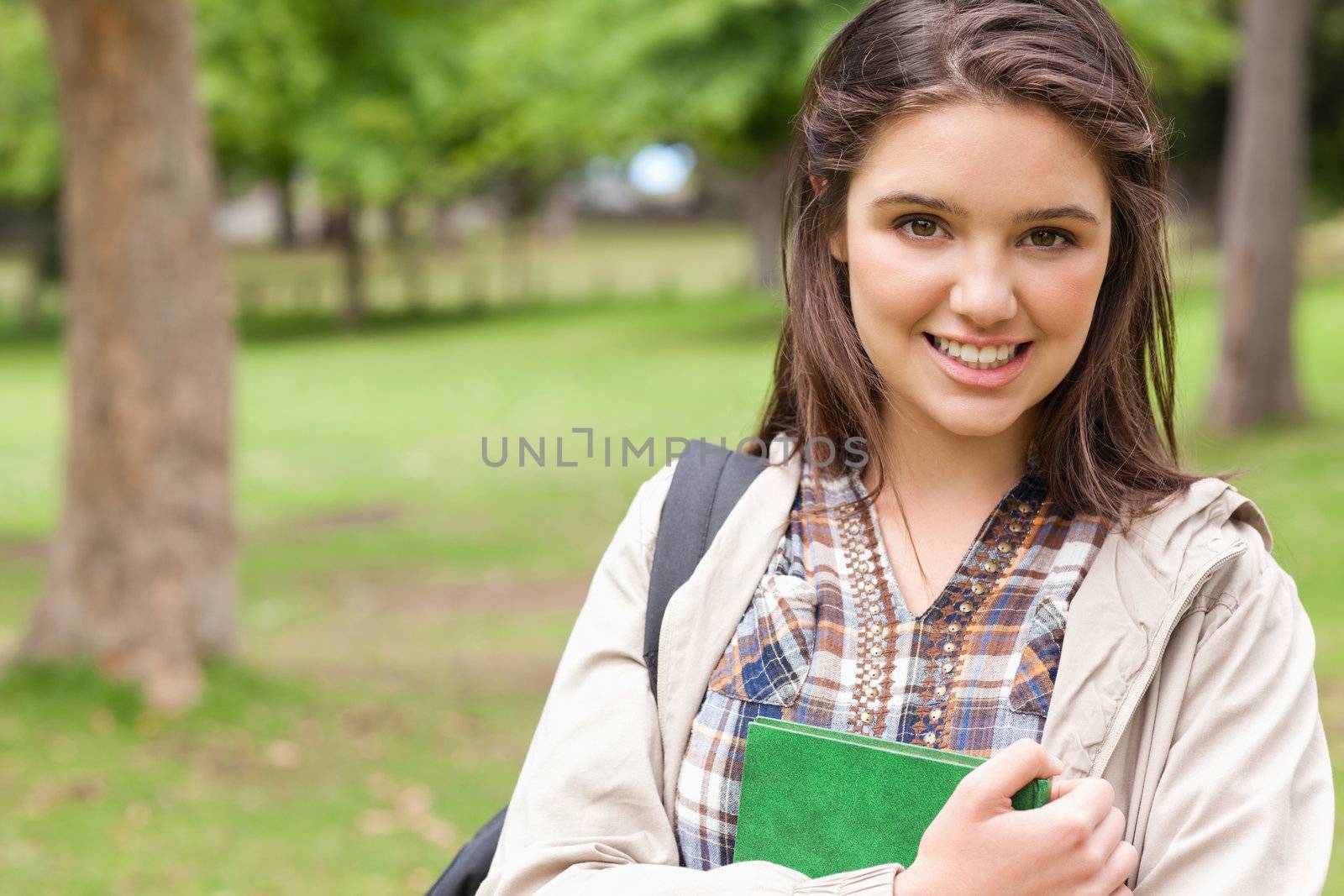 Portrait of a first-year student holding a textbook while posing in a park