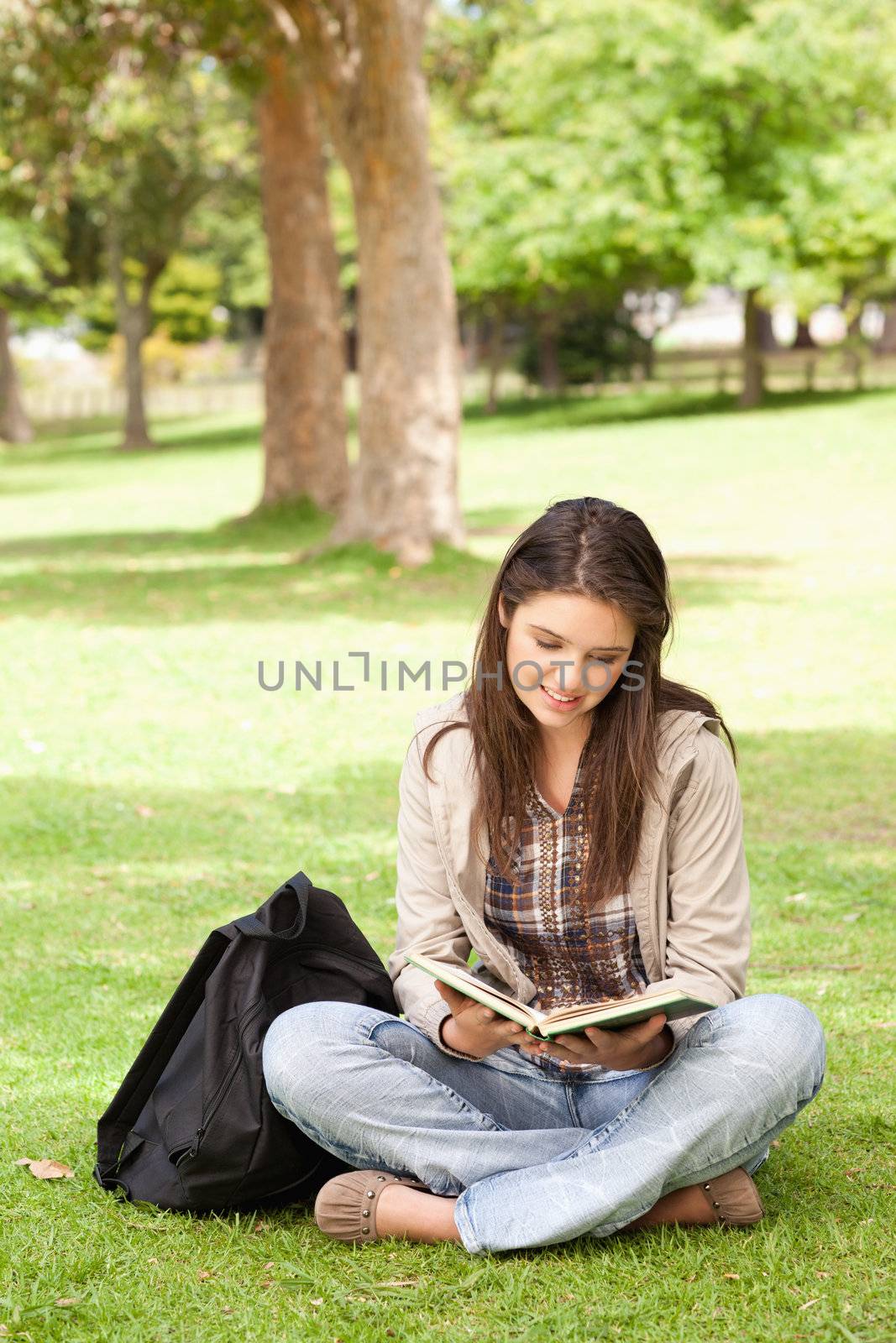 Teenager sitting while reading a textbook in a park