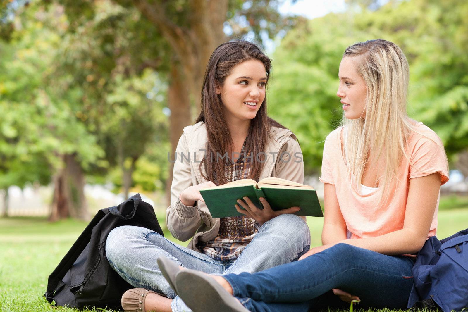 Female teenagers sitting while studying with a textbook in a park