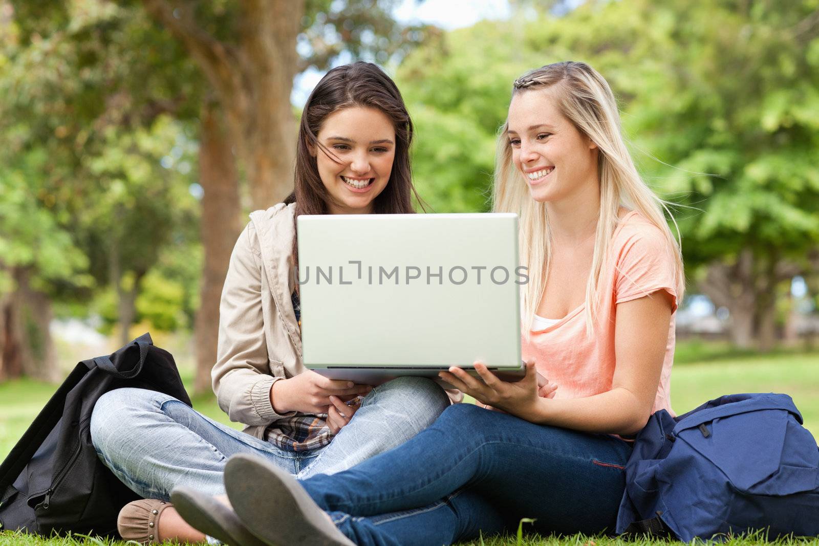 Happy teenagers sitting while using a laptop in a park