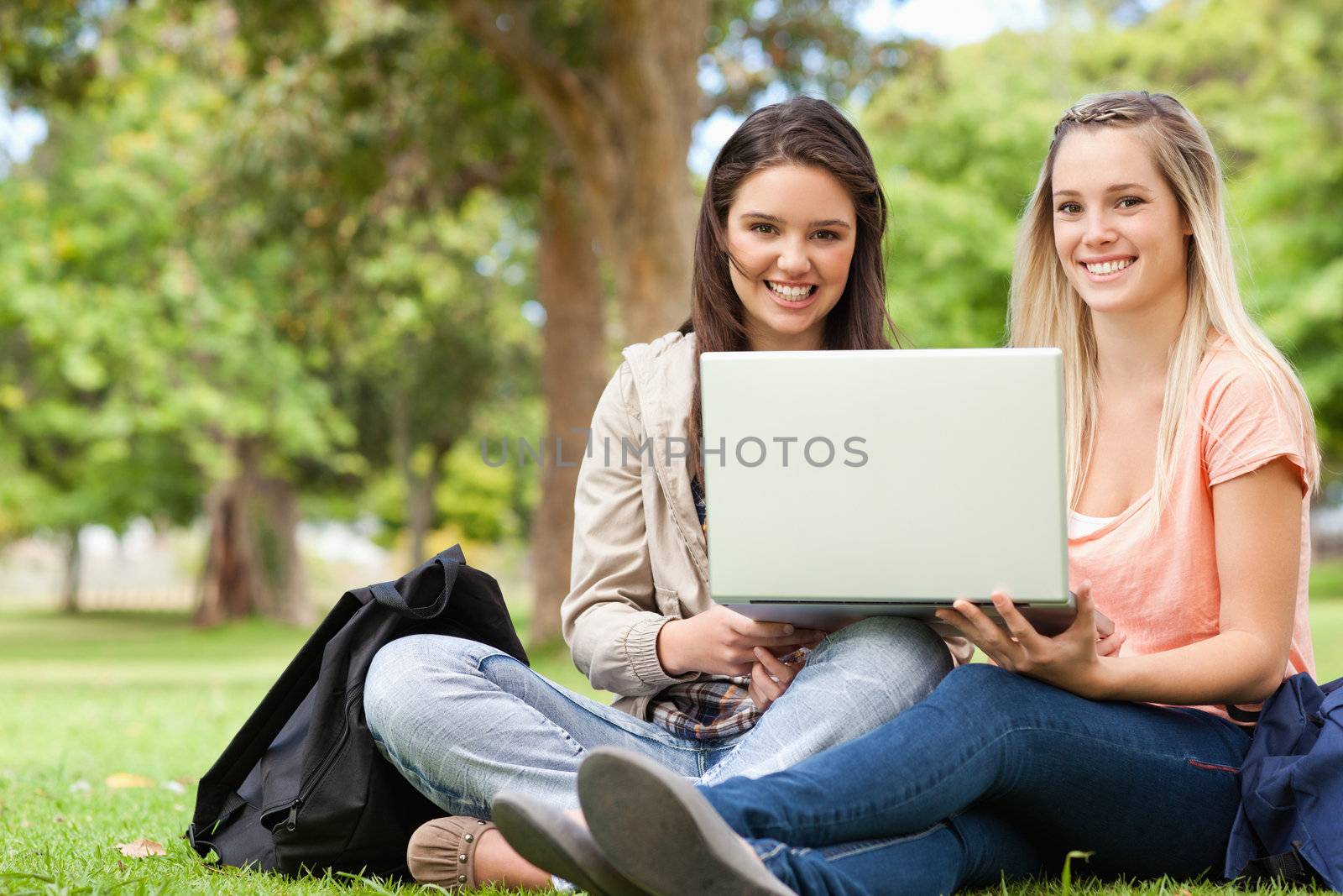 Smiling teenagers sitting while using a laptop by Wavebreakmedia