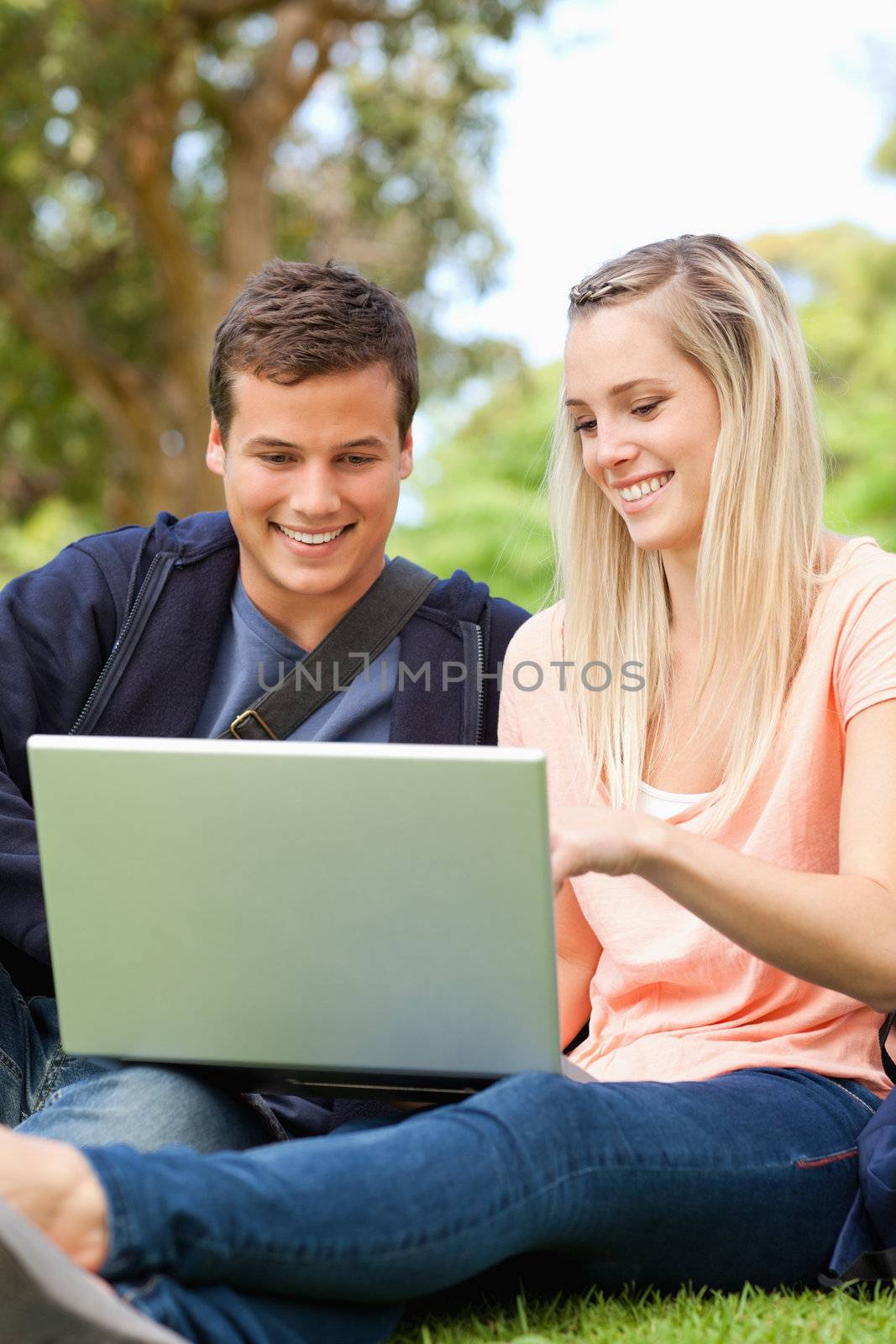 Close-up of young people sitting while using a laptop in a park