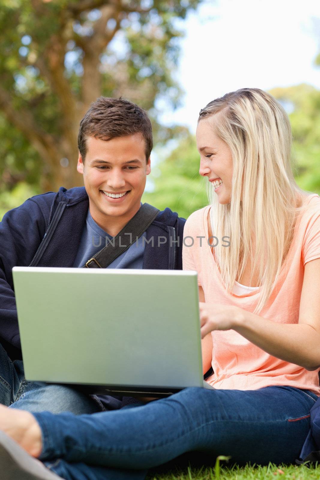 Close-up of young people laughing while sitting with a laptop in a park