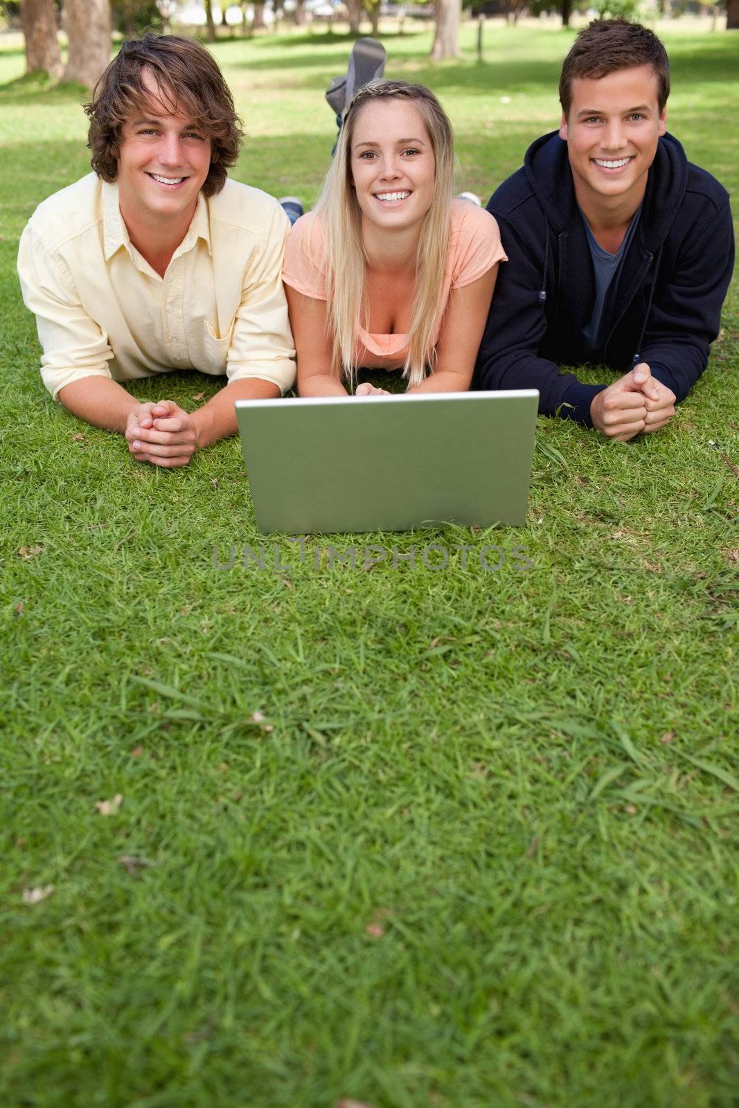 Three smiling students with a laptop in a park