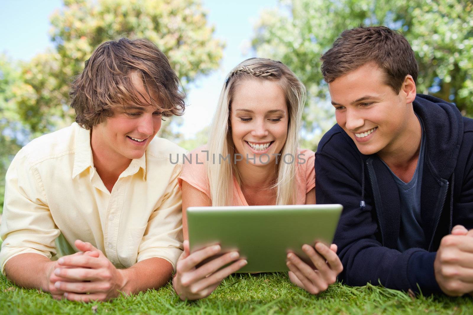 Three students using a tactile tablet while lying in a park