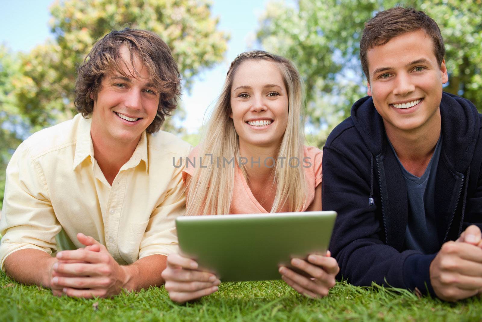 Three smiling students using a tactile tablet while lying in a park
