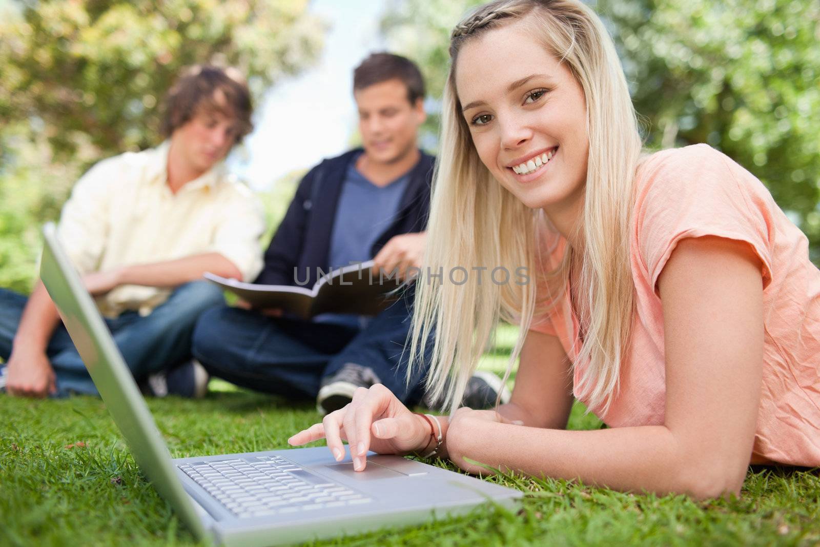 Portrait of a girl using a laptop while lying in a park with friends in background