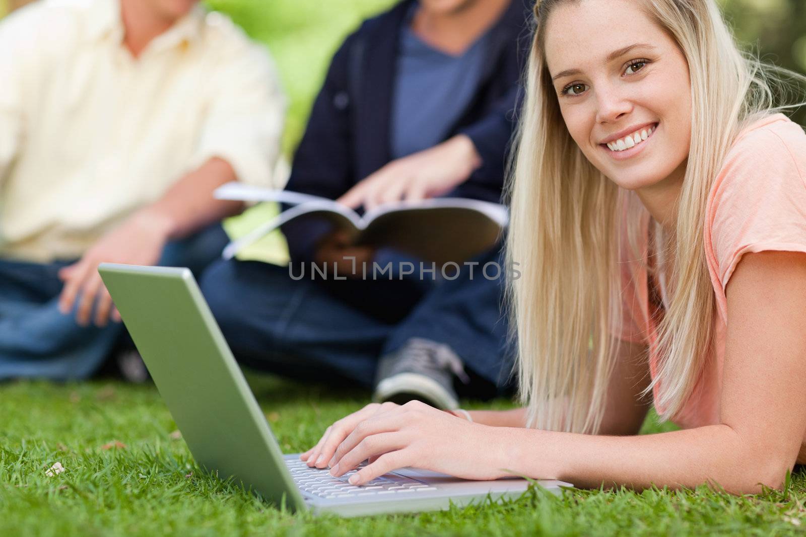 Portrait of a smiling girl using a laptop while lying in a park by Wavebreakmedia