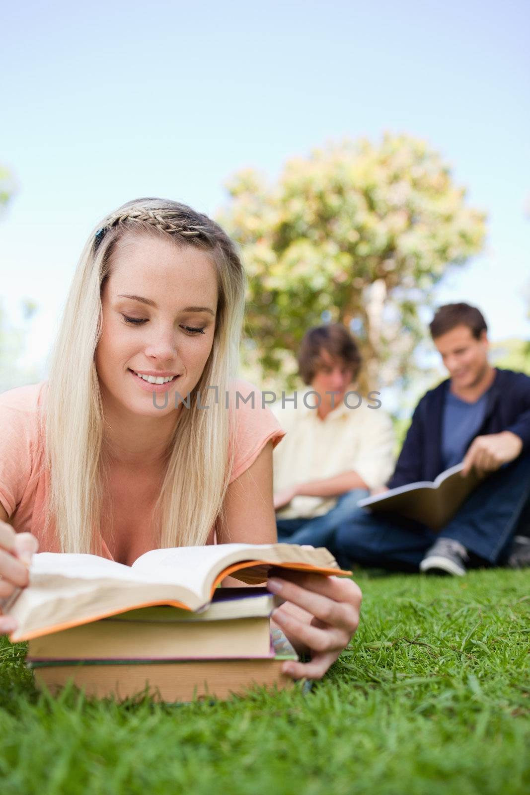 Close-up of a girl lying while reading books in a park with friends in background