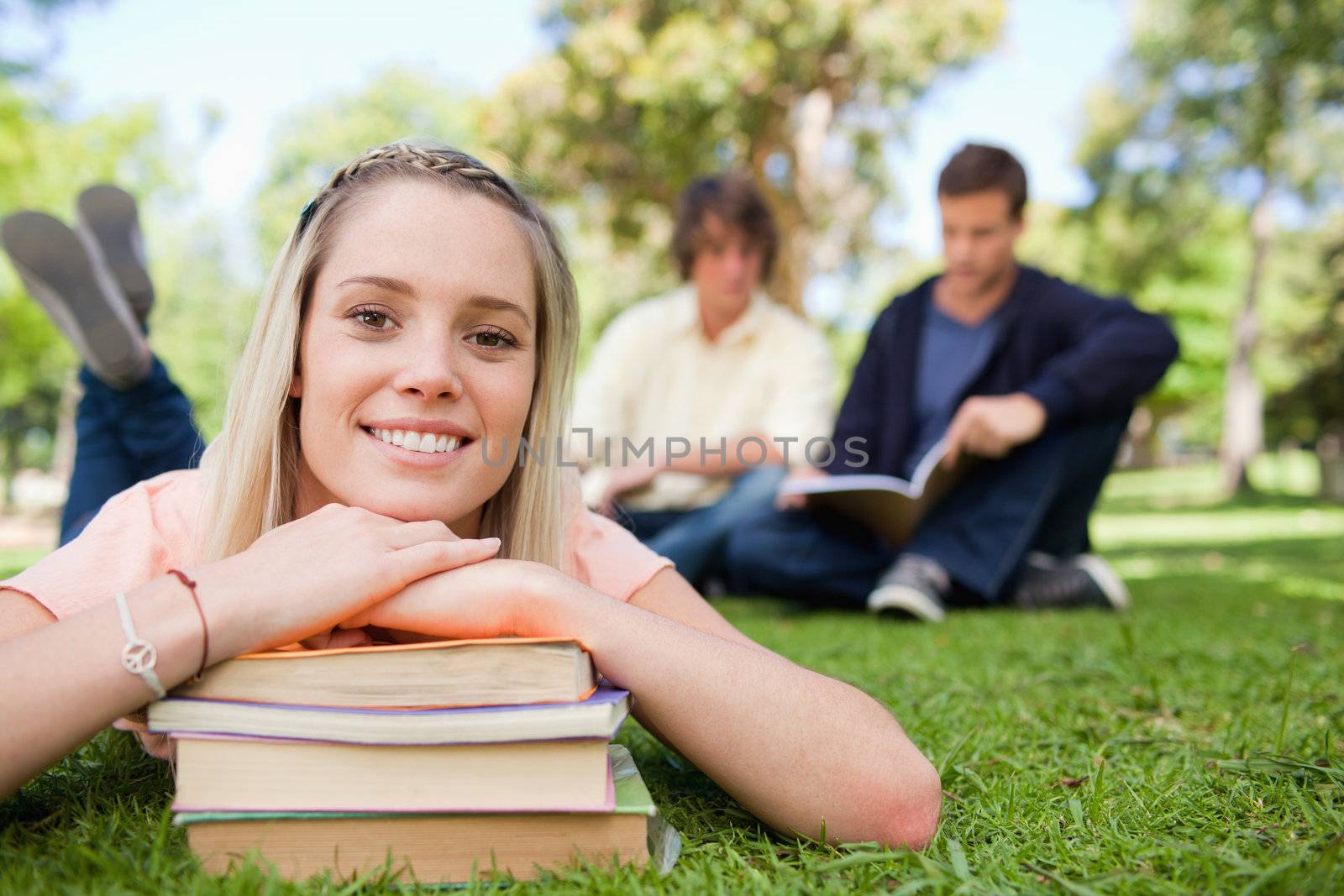 Porrtait of a girl lying head on her books in a park with friends in background