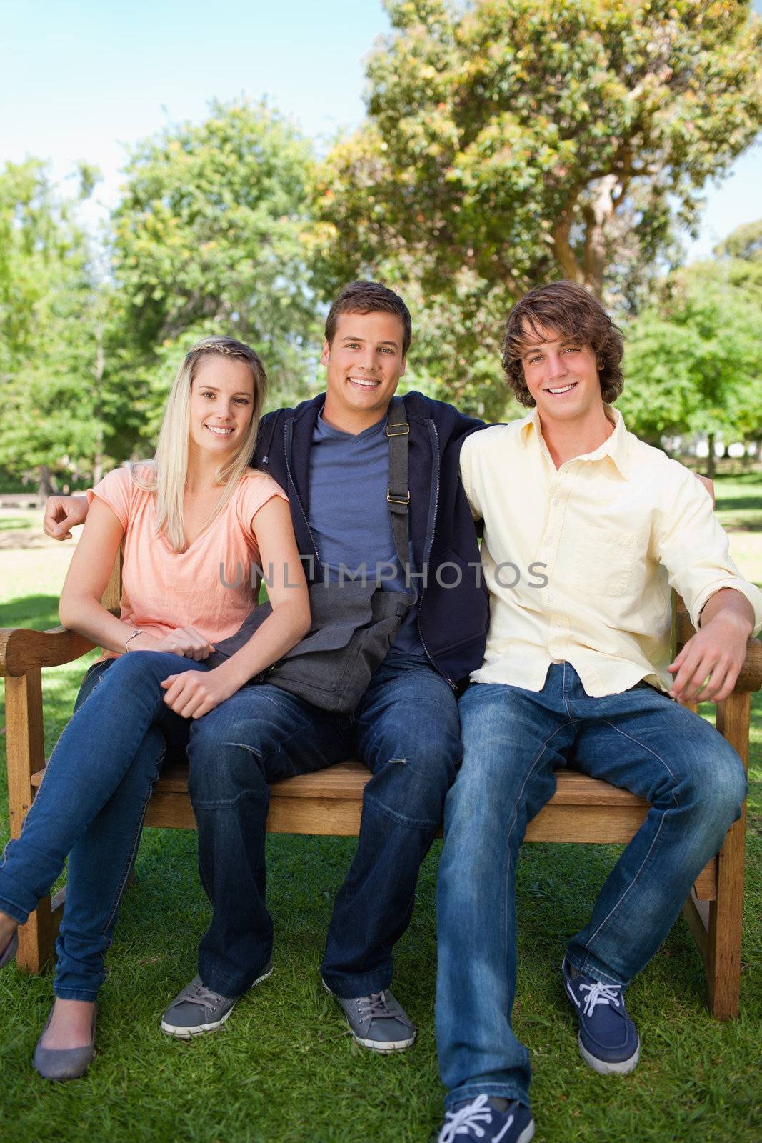 Three smiling students on a bench in a park together