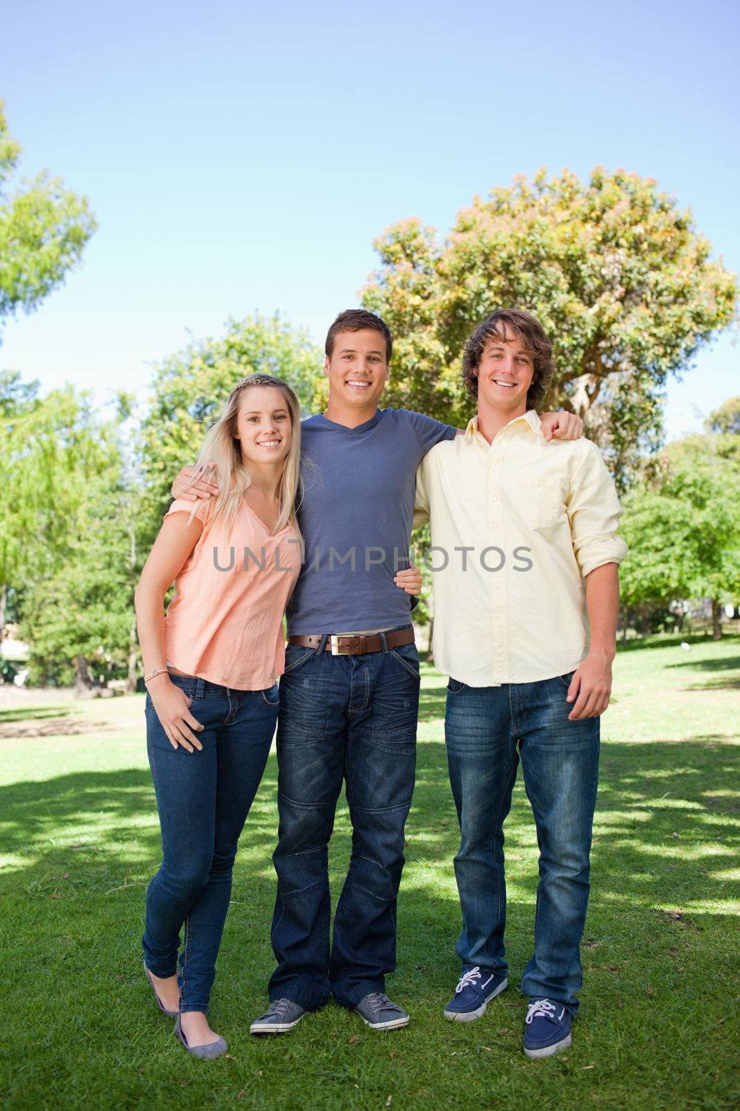 Three smiling students standing in a park together
