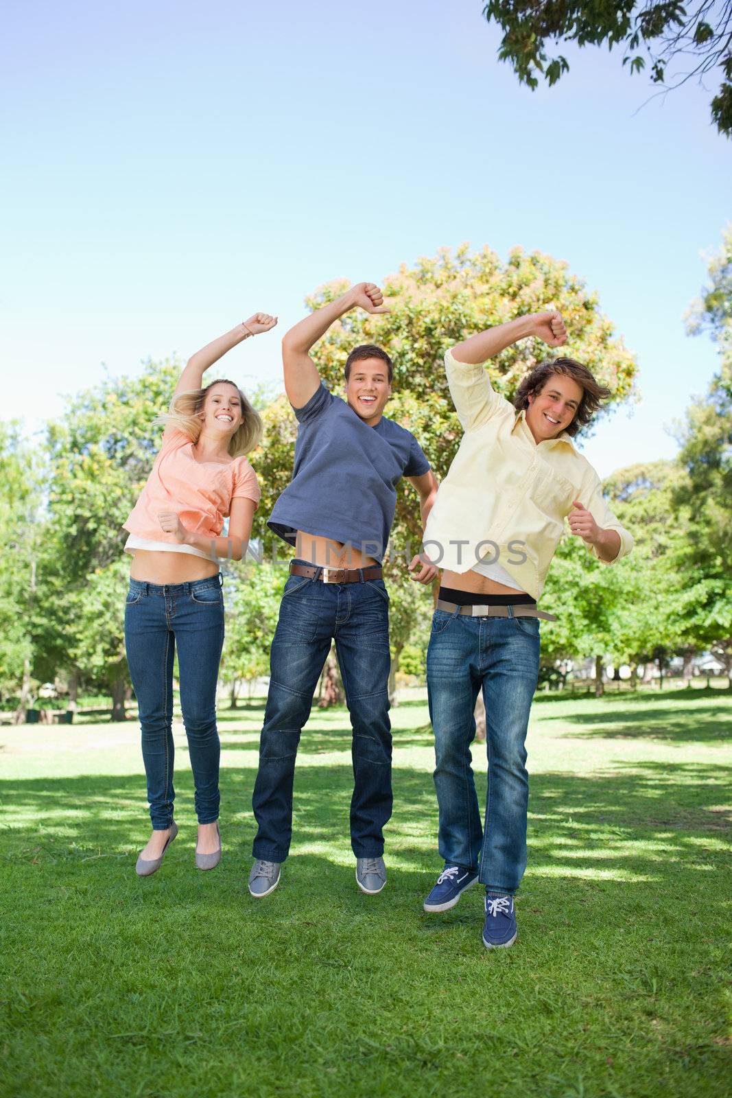 Three students jumping while raising an arm in a park