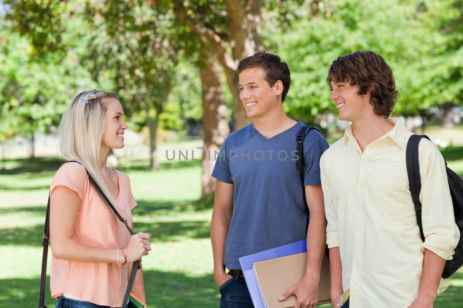 Girl speaks to two students in a park