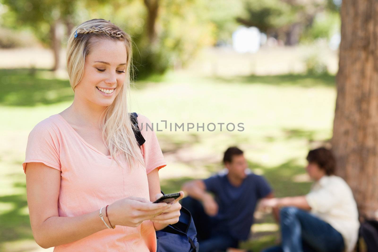 Close-up of a smiling girl using a smartphone in a park with friends in background