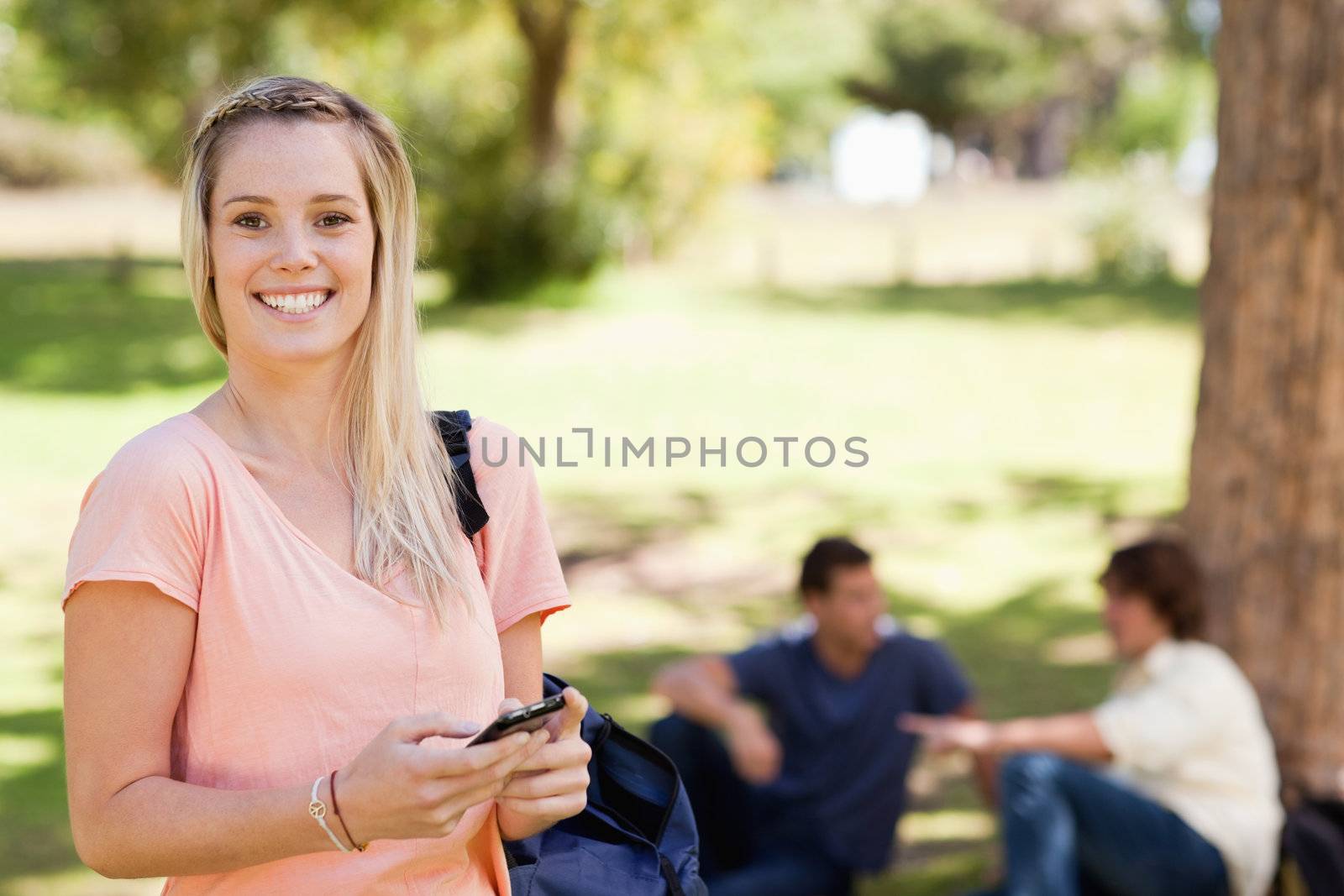 Portrait of a smiling girl using a smartphone in a park with friends in background