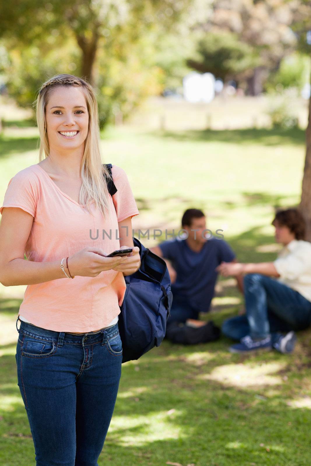 Portrait of a happy girl using a smartphone in a park with friends in background