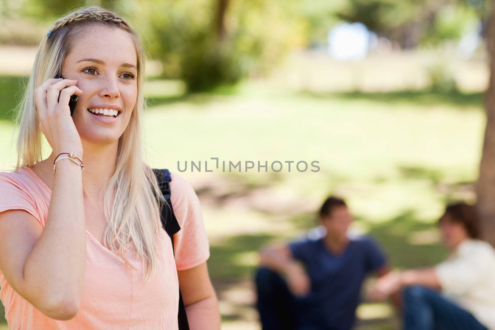 Close-up of a student on the phone in a park with friends in background