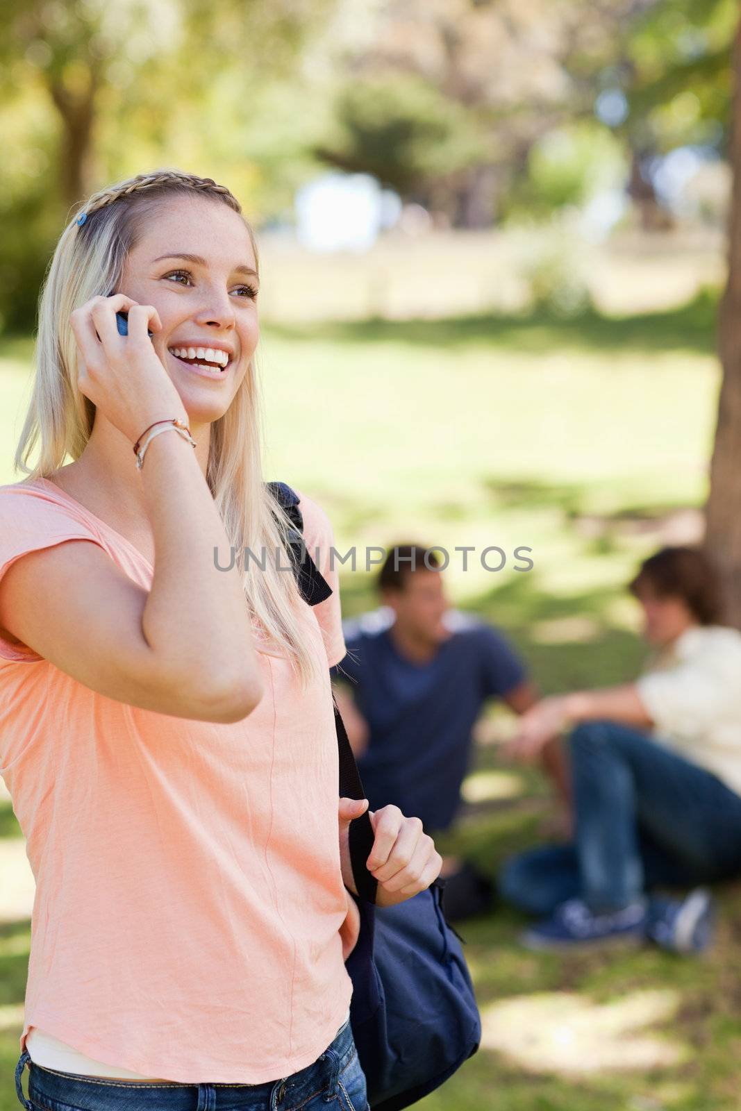 Teenager on the phone in a park with friends in background