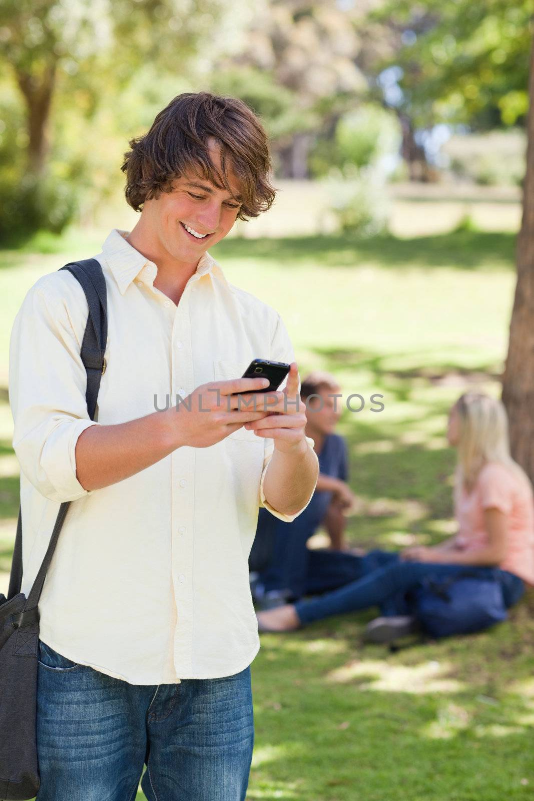 Young man using a smartphone in a park with friends in background