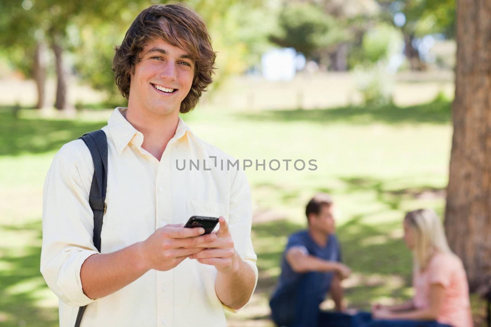 Portrait of a young man holding a smartphone in a park with friends in background
