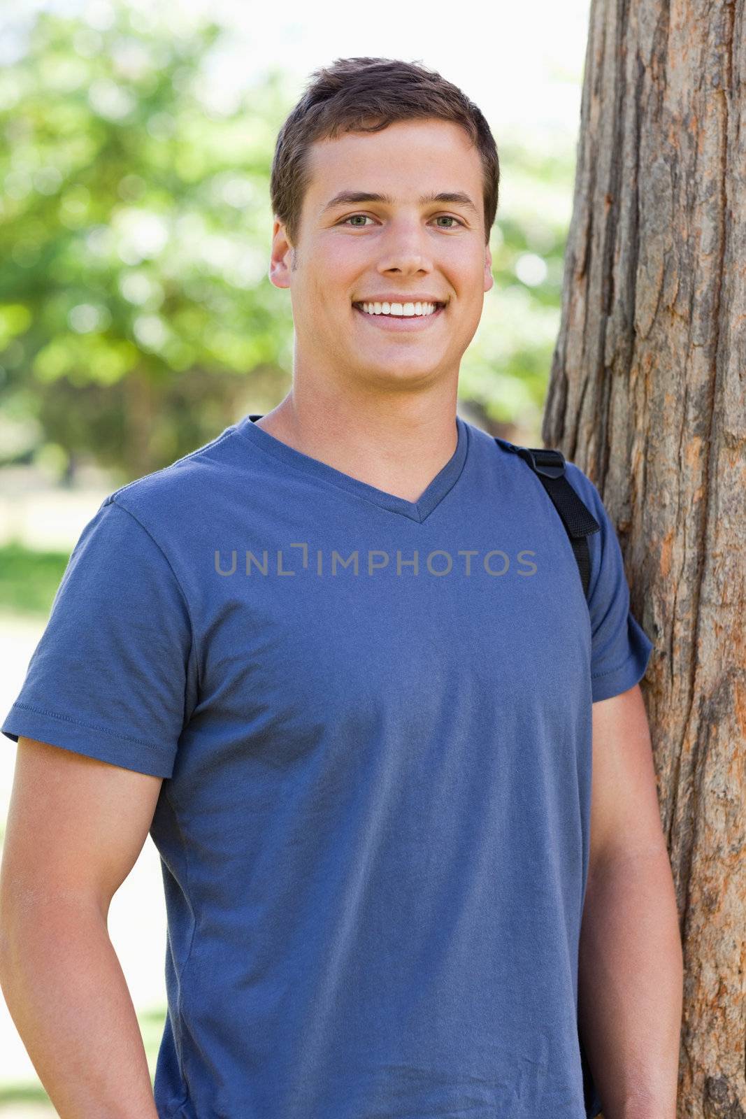 Close-up of a young man leaning against a tree in a park