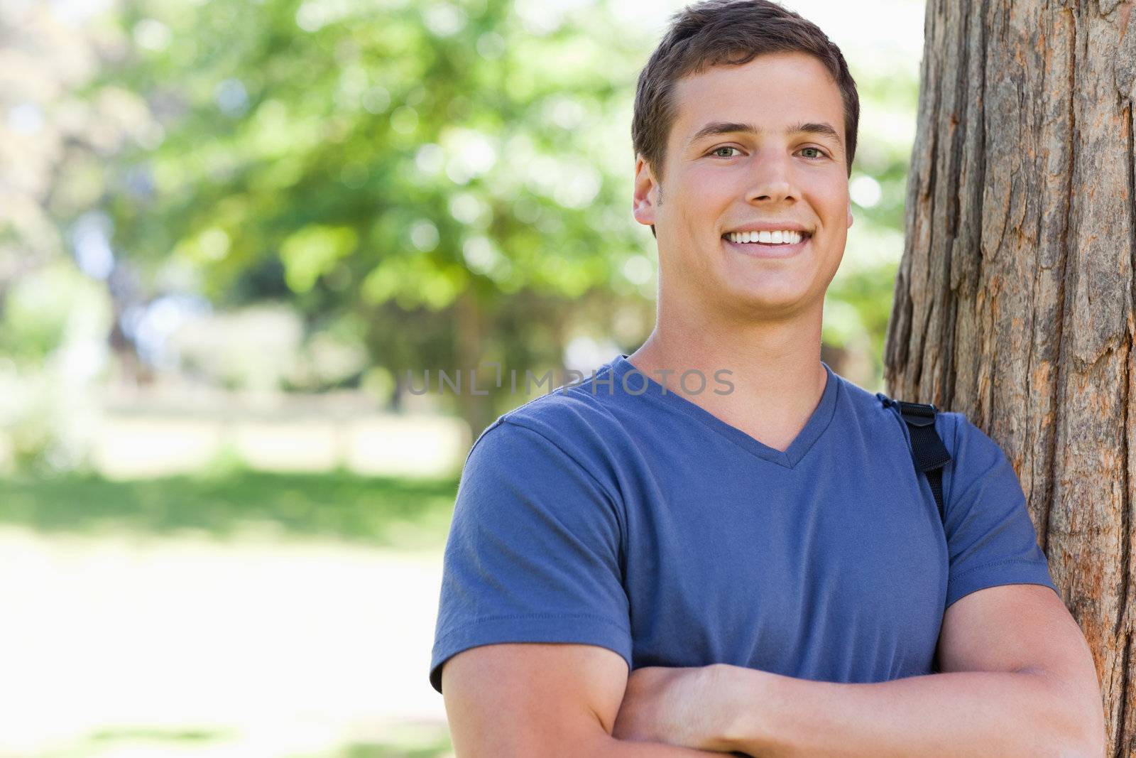 Portrait of a young man leaning against a tree in a park