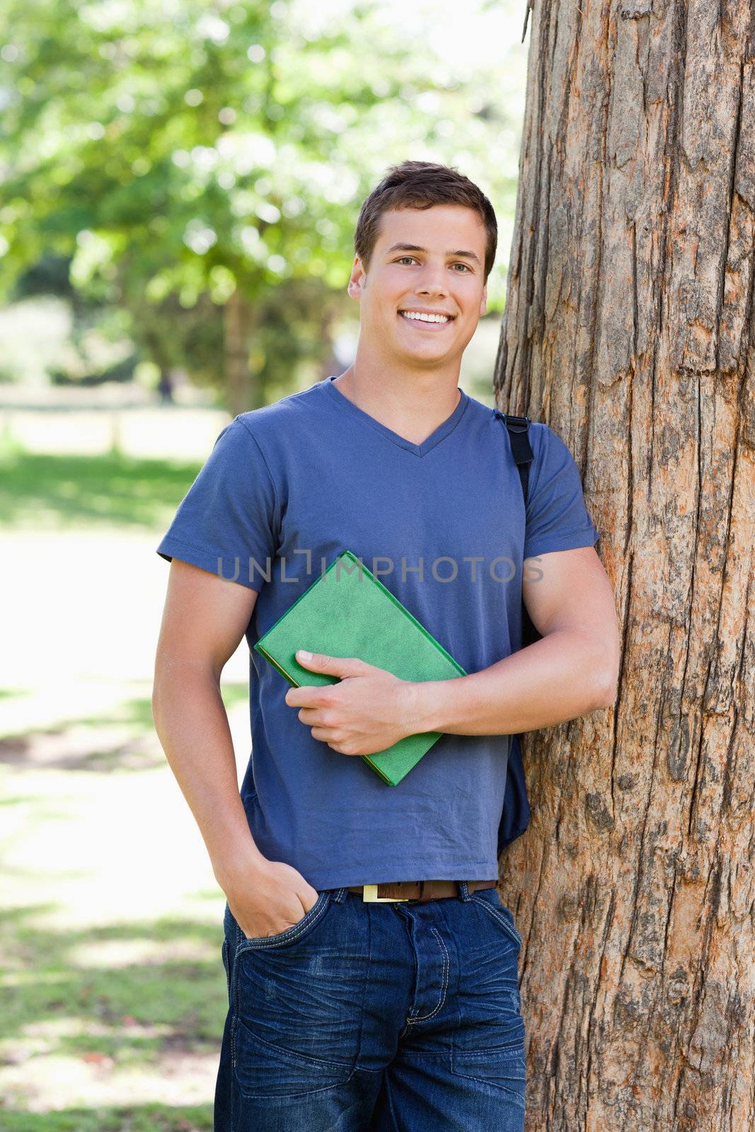 Portrait of a muscled student holding a textbook in a park