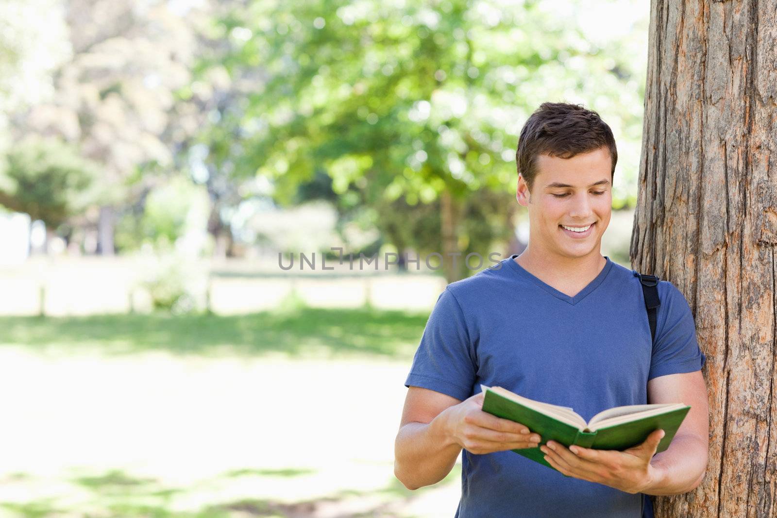 Muscled student holding a textbook in a park