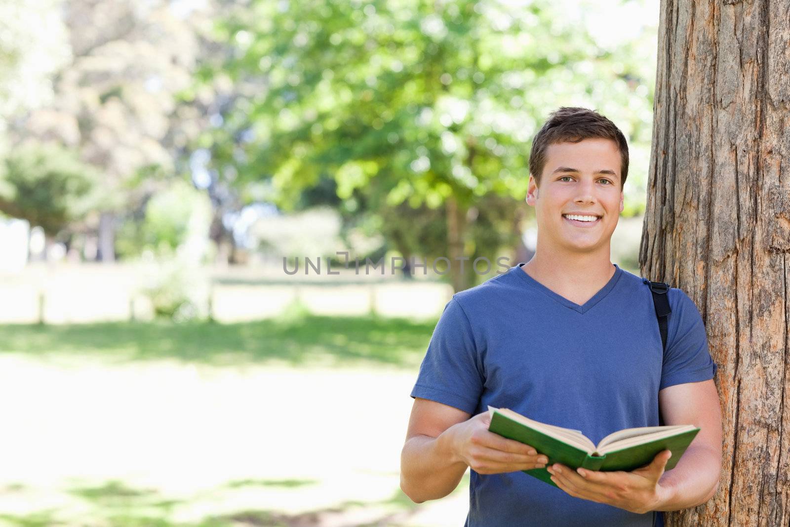 Portrait of a smiling toothy student holding a textbook in a park