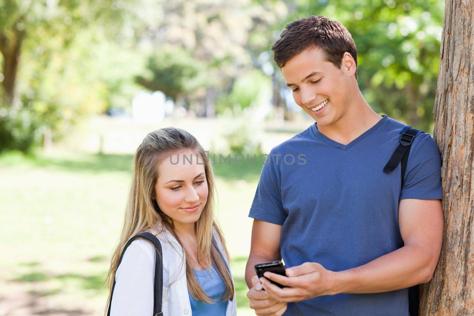 Close-up of a student showing his smartphone screen to a girl in a park
