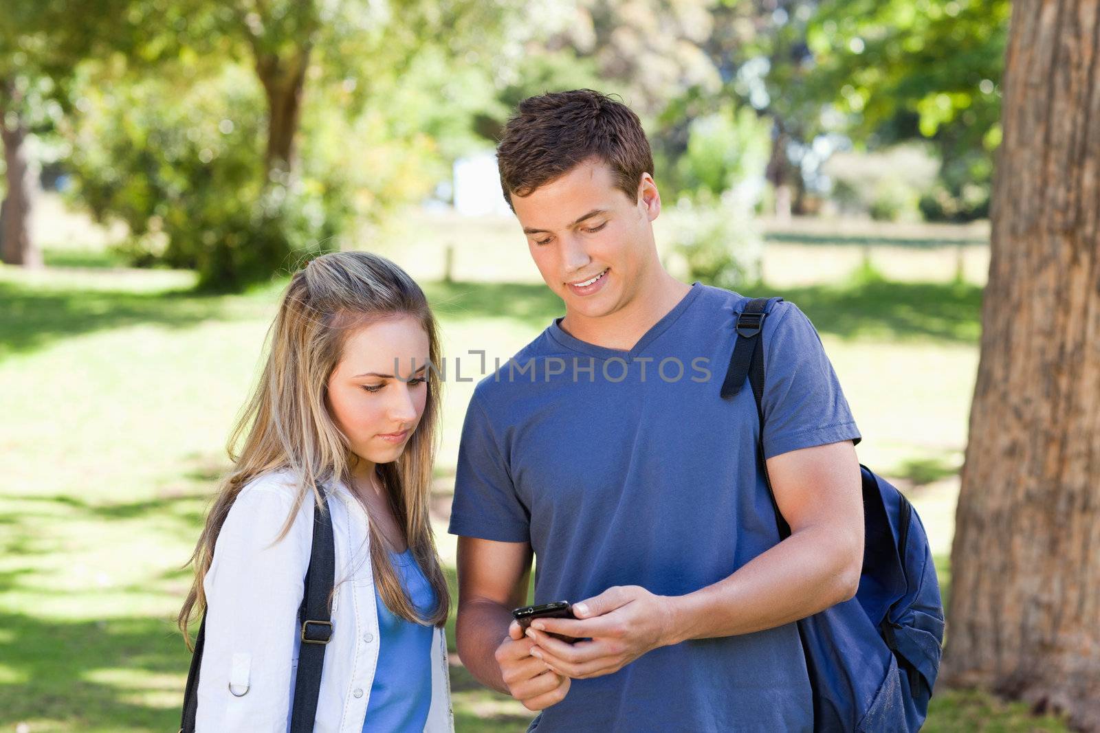 Close-up of a student showing his smartphone to a girl in a park