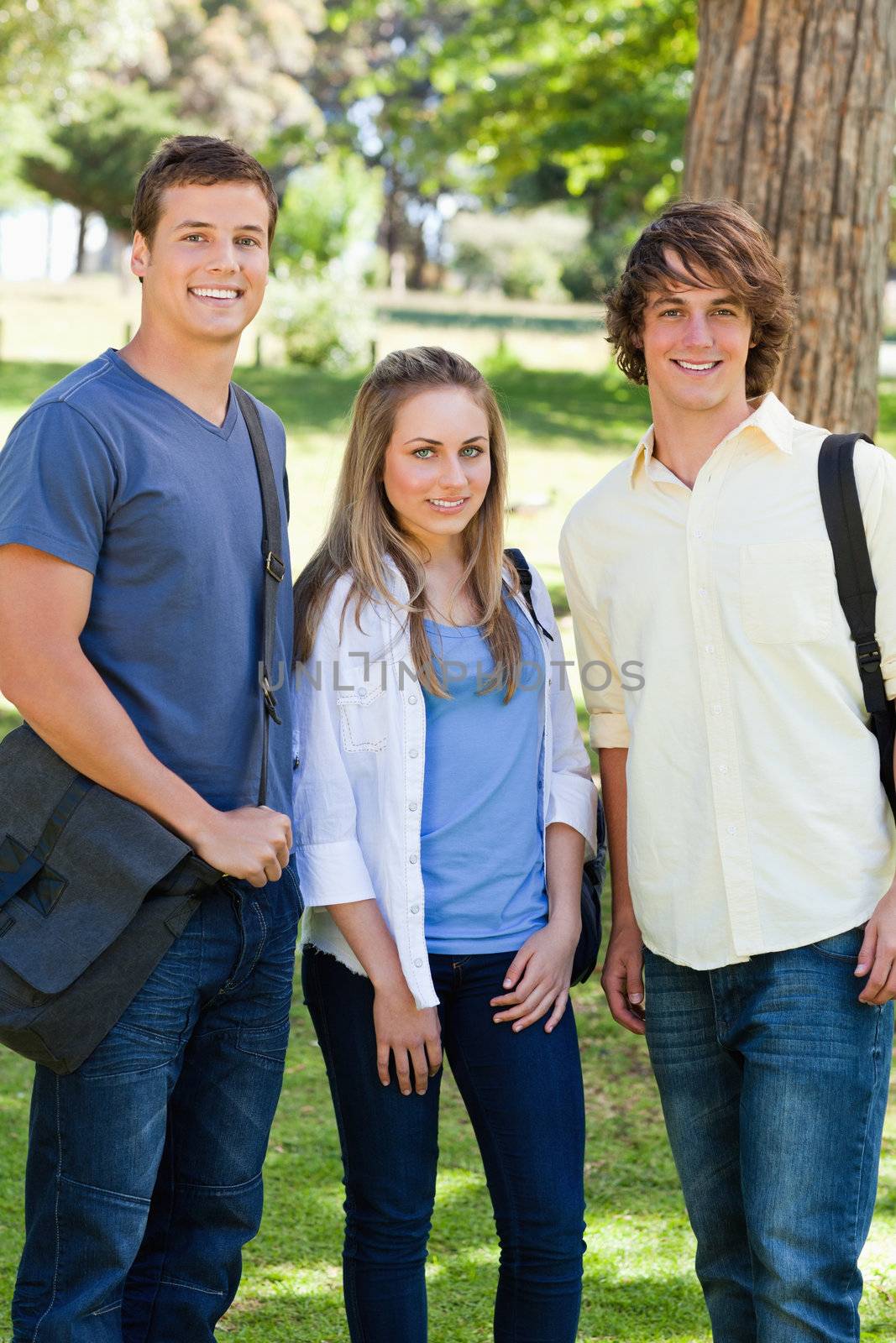 Smiling students with their bags posing in a park