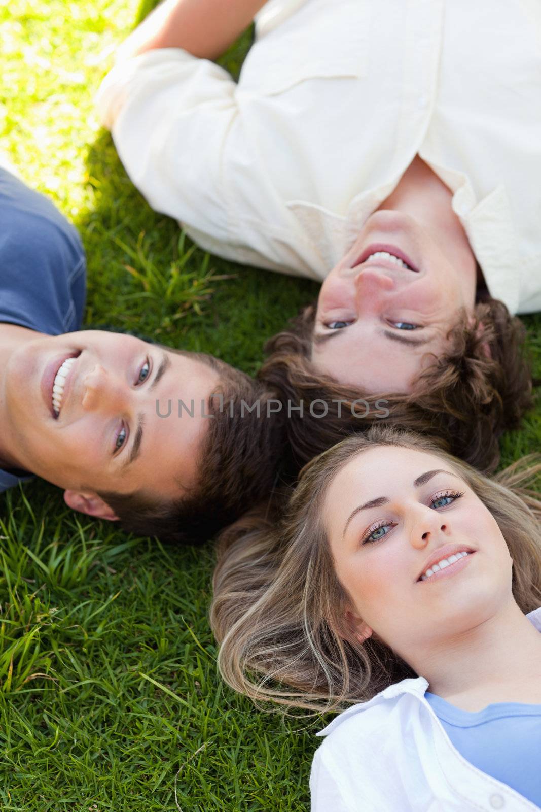 Three students resting together while looking at camera in the grass