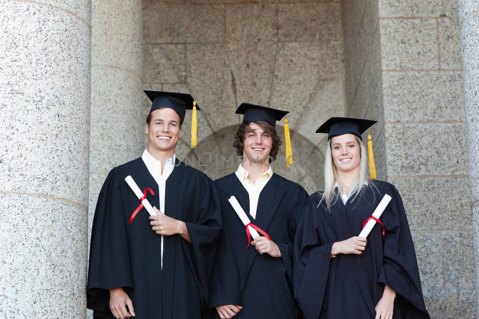 Portrait of graduates holding their diploma with university in backgroung