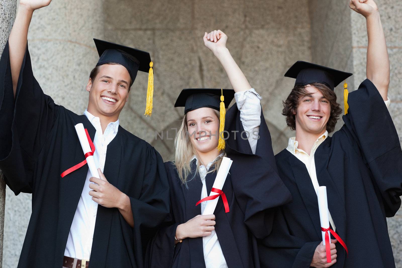 Graduates holding their diploma while raising arm by Wavebreakmedia