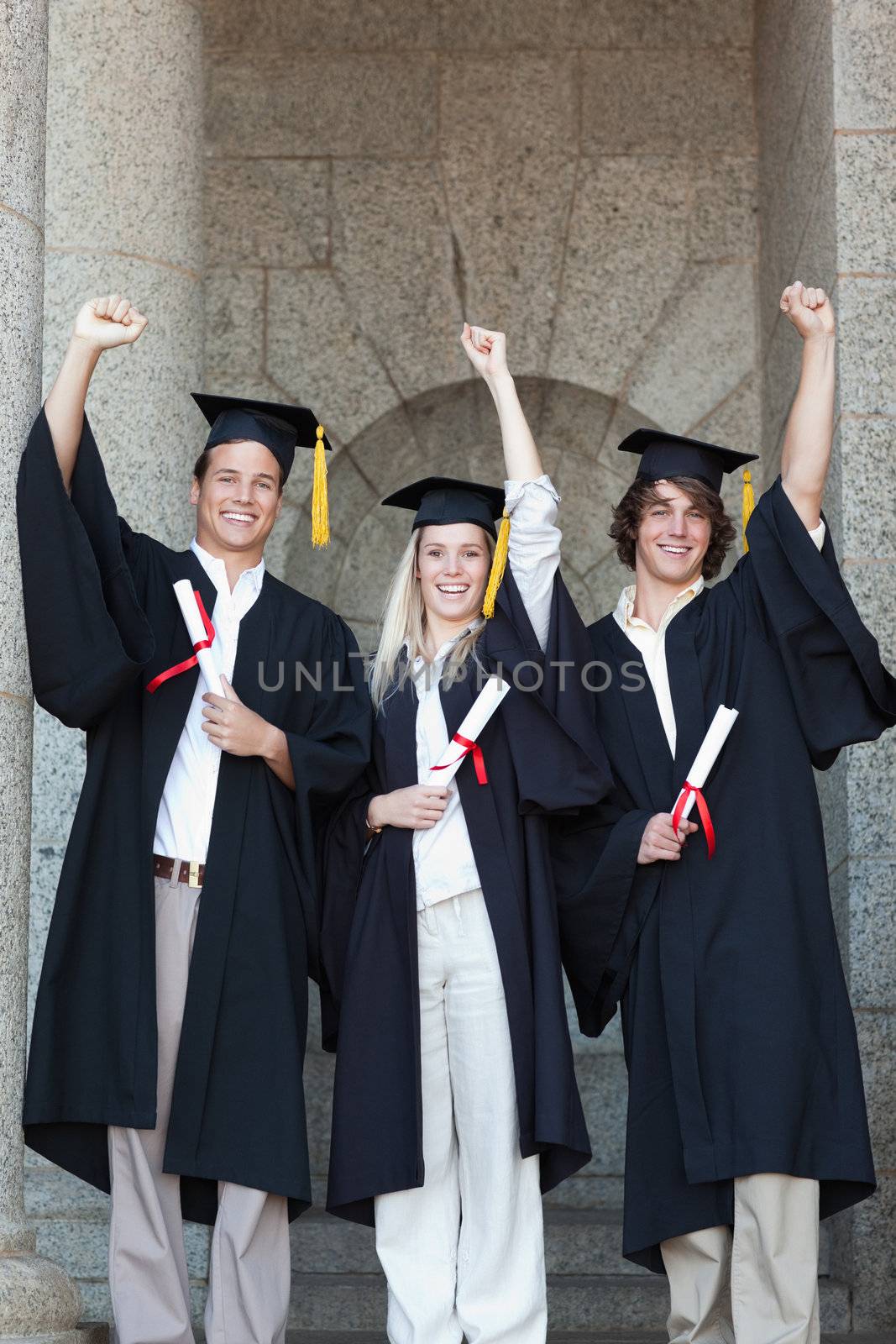 Happy graduates raising arm with university in backgroung