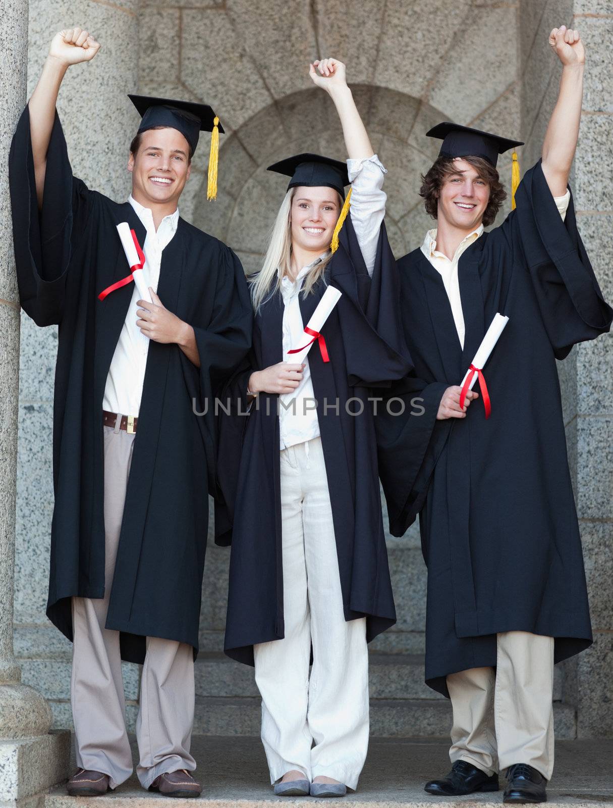 Smiling graduates raising arm with university in backgroung