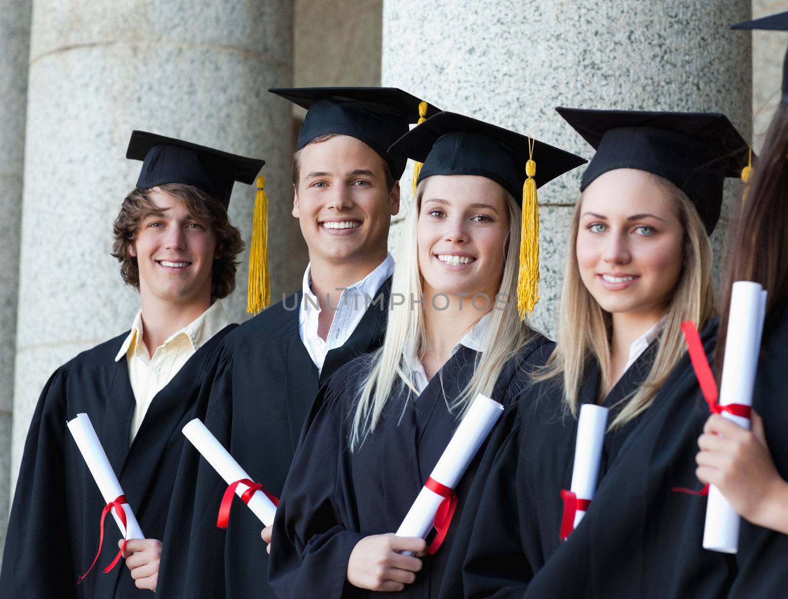 Portrait of smiling graduates posing in single line with columns in background