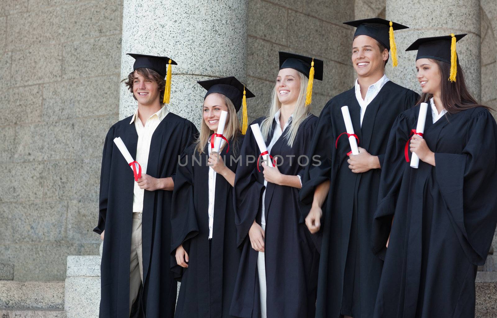 Smiling graduates posing while holding their diploma in front of the university