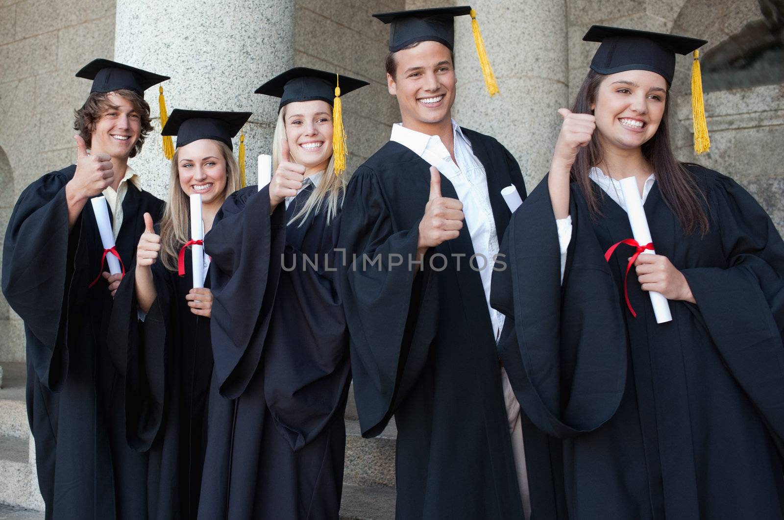 Graduates posing the thumb-up in front of the university