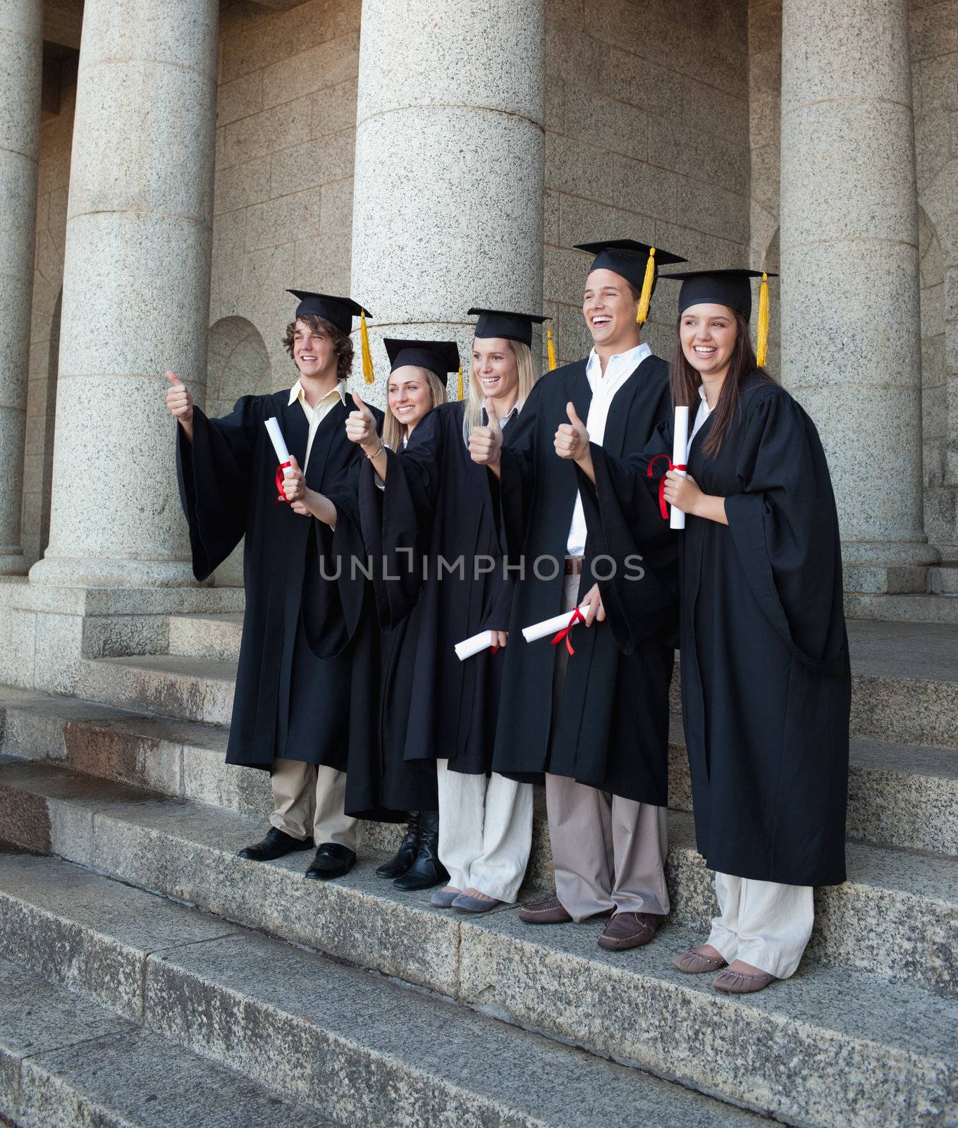 Laughing graduates posing the thumb-up by Wavebreakmedia