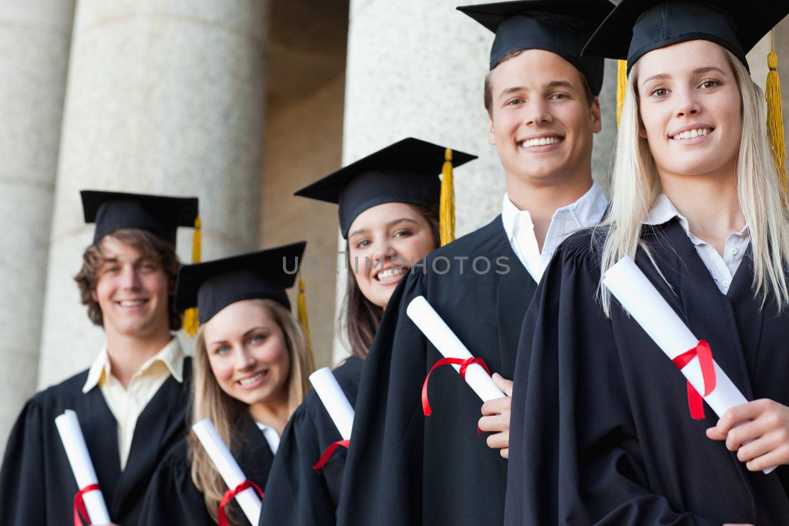 Close-up of five graduates posing in front of the university