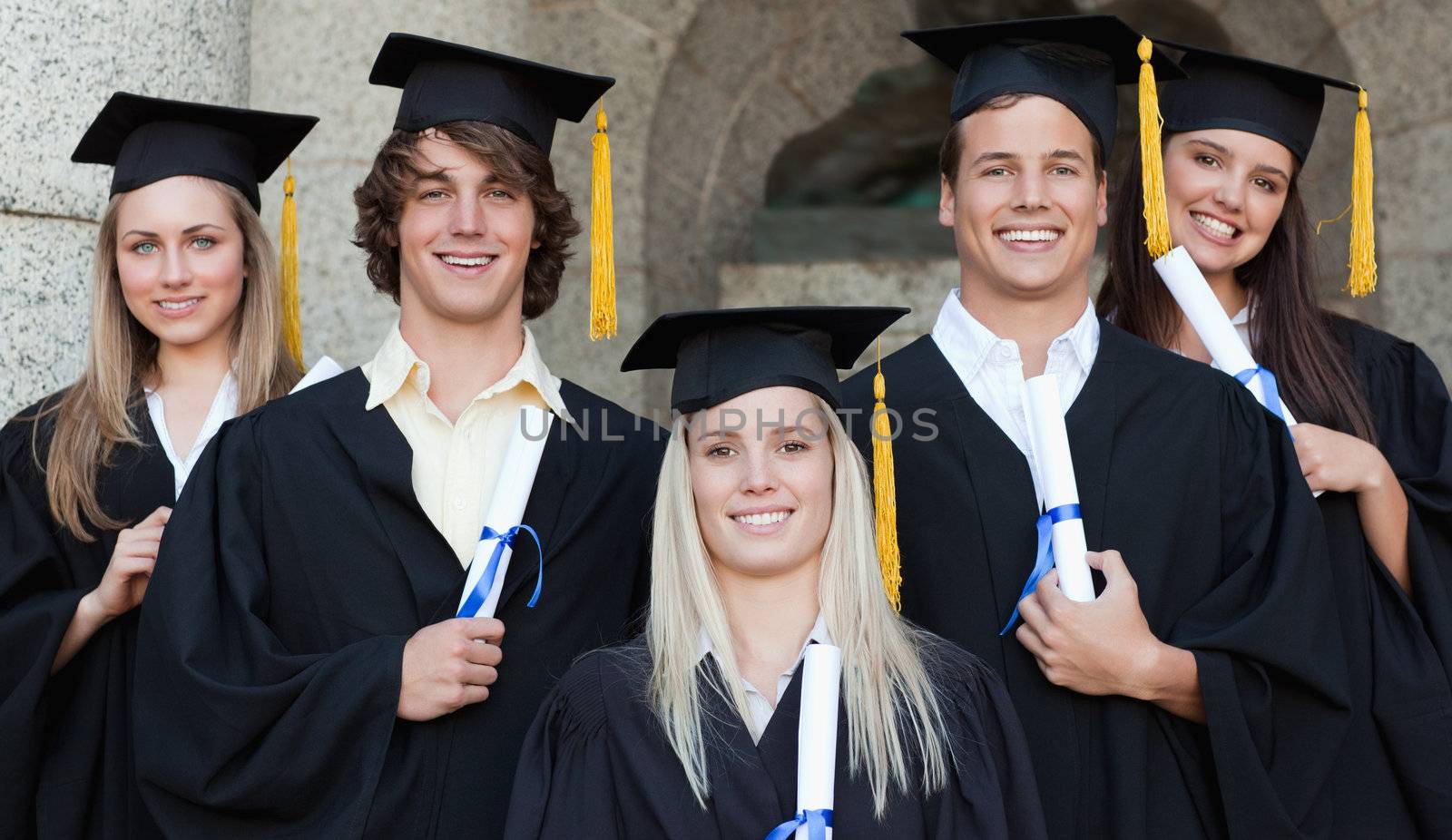 Close-up of five happy graduates posing in front of the university