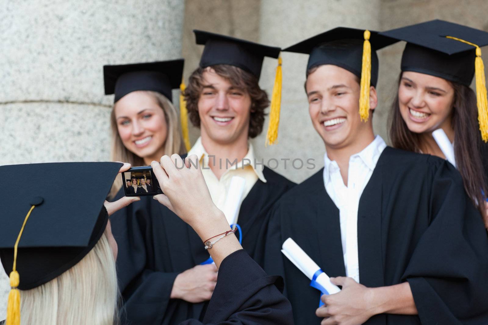 Close-up of a graduate taking a picture of her smiling friend in front of the university